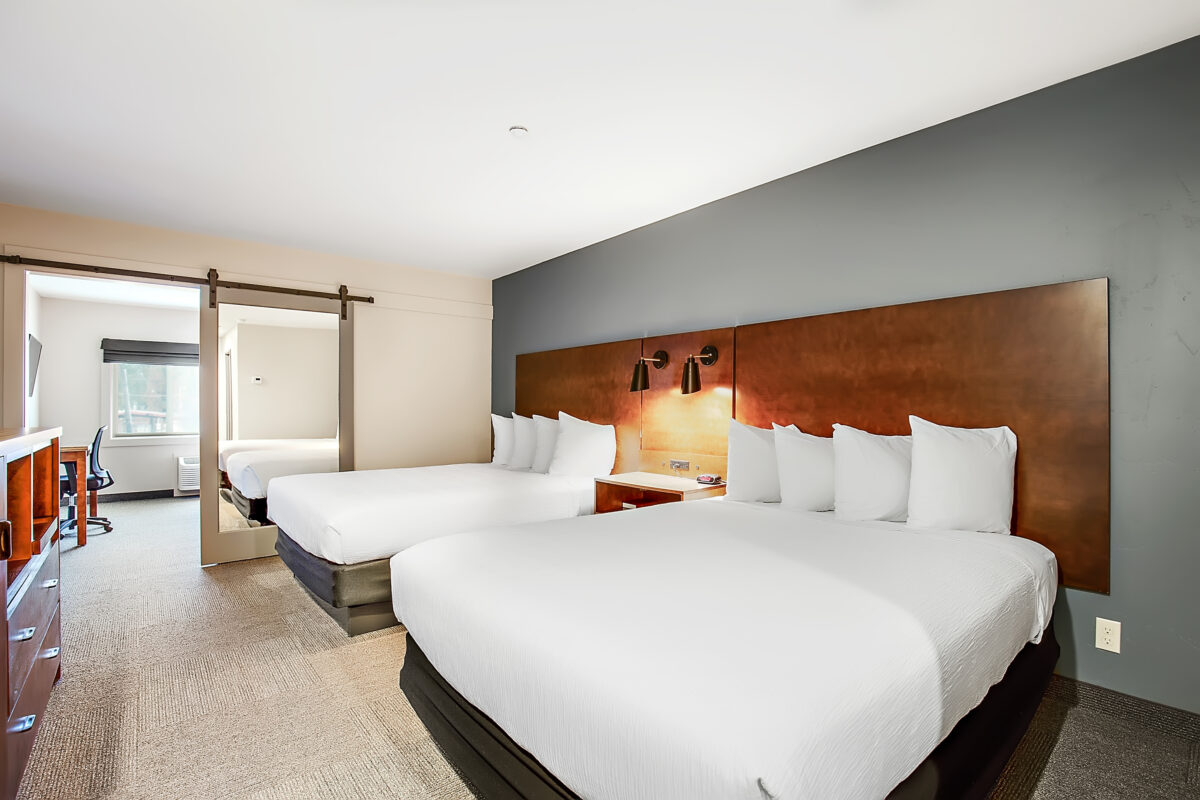 A hotel room with two queen beds, a wooden headboard, and a desk area.